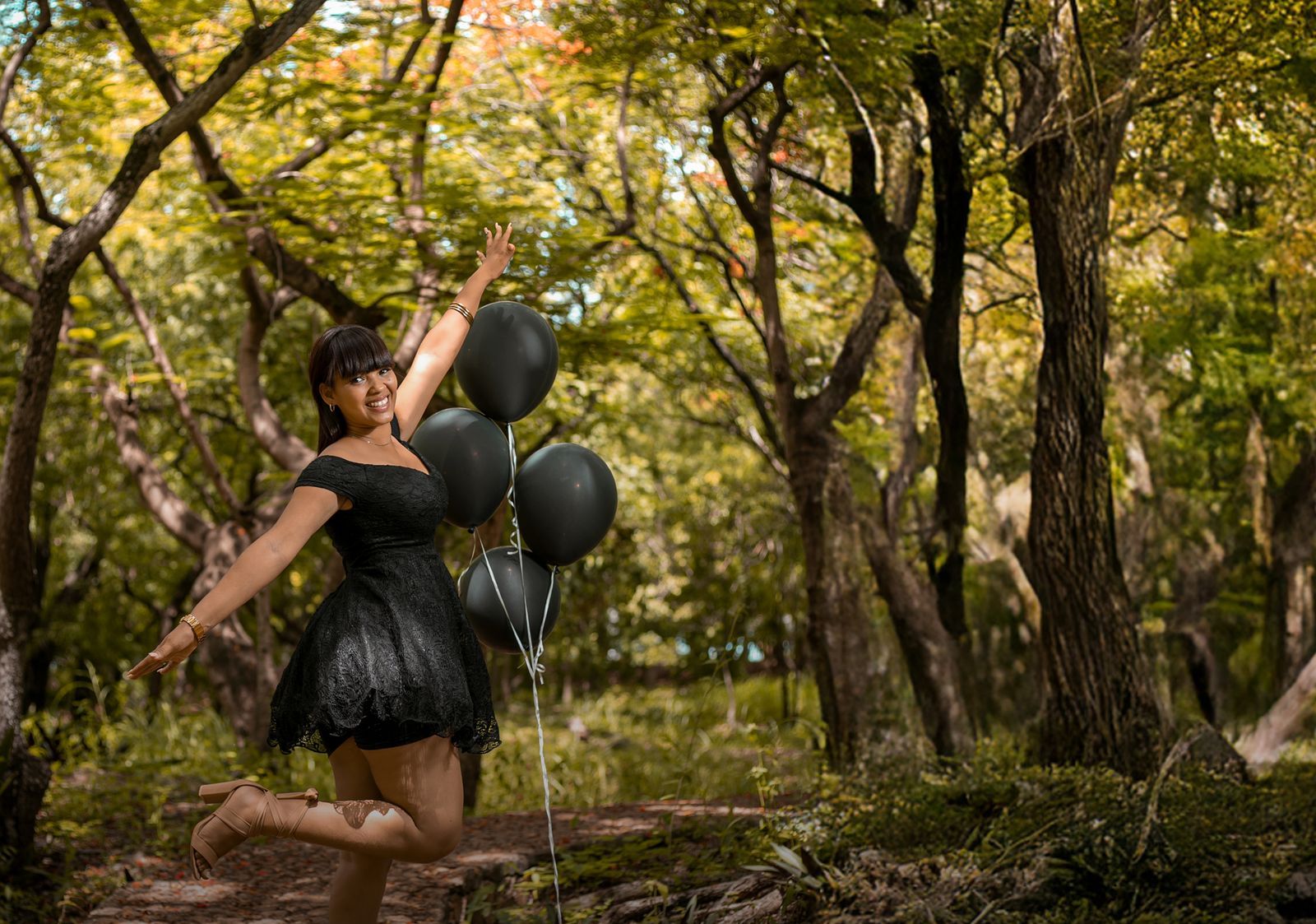 Joven saltando con globos negros en el bosque
